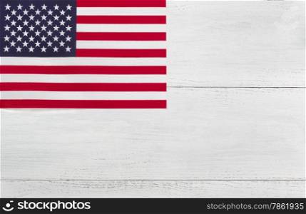 Top view angled shot of United States flag on white wooden boards in horizontal layout with flag in upper left hand corner.