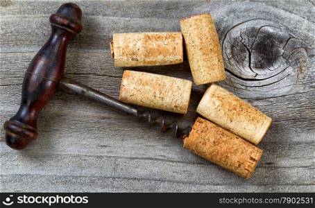 Top view angled shot of vintage corkscrew with five used corks on rustic wooden boards.