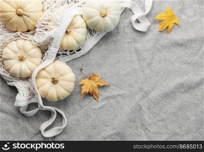 Top view autumn composition with pumpkins in mesh shopping bag on a grey textile  background