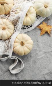 Top view autumn composition with pumpkins in mesh shopping bag on a grey textile  background