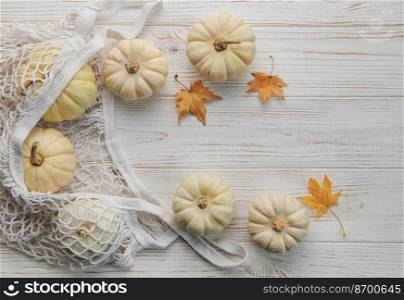 Top view autumn composition with pumpkins in mesh shopping bag on a wooden background