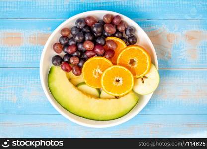 Top view black grapes, red grapes, Valencia orange and melon fruits in white dish on blue wood table. dieting healthy food and healthcare concept