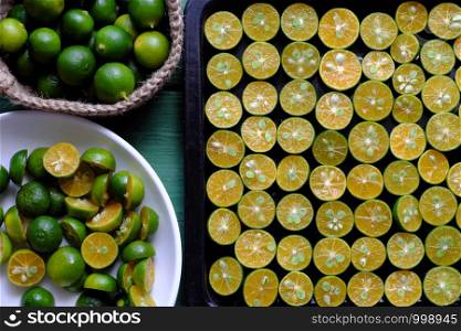 Top view black tray of many kumquat fruits cut in half with green peel and yellow flesh on green wooden background, this sour fruit rich vitamin c, healthy and make detox drink