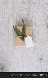 top view brown wrapped gift box with tag green leaves wooden table