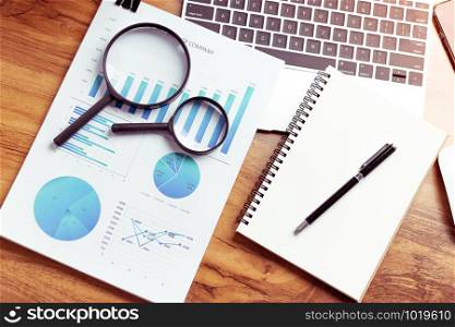 Top view,Business desk with a notebook, report graph chart, pen and tablet on wooden table