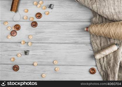 top view button string spool needle thimble cloth wooden background