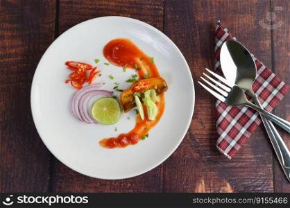 Top View canned sardine with tomato sauce and cooking ingredient was beautiful arrangement in white plate, stainless spoon and fork on napkin placed nearly on wooden table