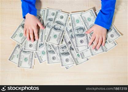 Top view, close-up of hands counting money. Happy child with money dollar, little businessman. Pile of United States dollar hundred USD banknotes in boy&rsquo;s hand.. Close-up of hands counting money. Happy child with money dollar, little businessman. Pile of United States dollar hundred USD banknotes