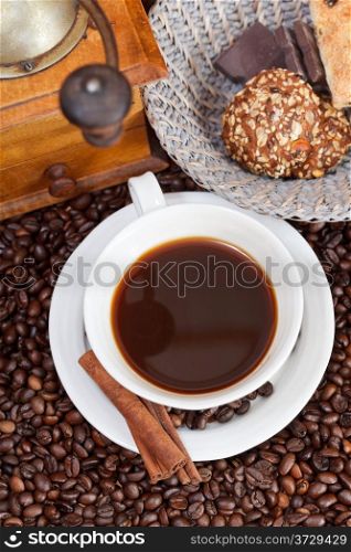 top view cup of coffee and roasted coffee beans with retro wooden manual mill, biscuit, chocolate bars, cinnamon