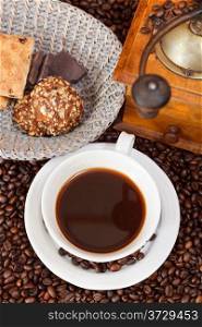 top view cup of coffee and roasted coffee beans with retro wooden manual mill, biscuit, chocolate bars