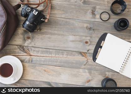 top view dslr camera cup tea spiral notepad pen camera lens bag wooden table