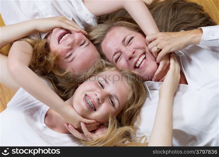 Top view, facing forward, of mother and her daughters lying on oak wooden floor while all joining hands and faces together
