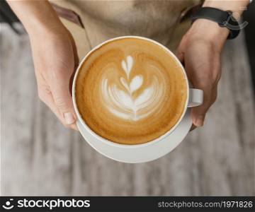 top view female barista holding decorated cup coffee hands. High resolution photo. top view female barista holding decorated cup coffee hands. High quality photo