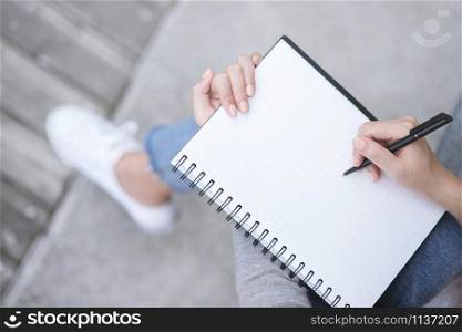 Top view female hands with pen writing on notebook notepad sitting in public park outdoor. Leave copy space empty write a message.