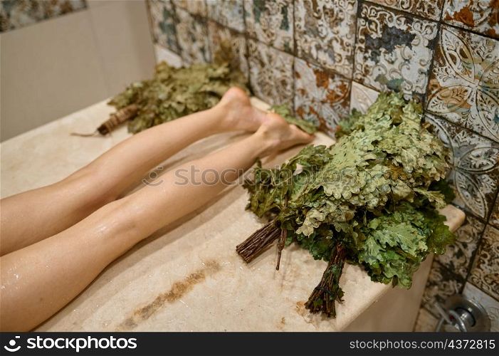 Top view female leg on wooden bench. Woman rest in spa sauna or russian bath with oak broom. Top view female leg on wooden bench