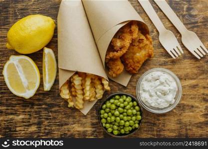 top view fish chips paper wrap with peas cutlery