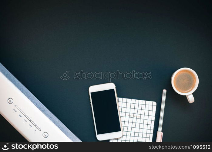 Top view flat lay of feminine desk workspace with white stereo bluetooth soundbar and smartphone for music listening and coffee cup with copy space on black background. Template for blog social media