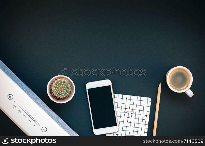 Top view flat lay of feminine desk workspace with white stereo bluetooth soundbar and smartphone for music listening and coffee cup with copy space on black background. Template for blog social media