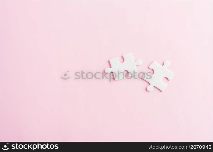 Top view flat lay of two paper plain white jigsaw puzzle game last pieces for solve, studio shot on a pink background, quiz calculation concept