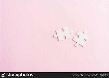 Top view flat lay of two paper plain white jigsaw puzzle game last pieces for solve, studio shot on a pink background, quiz calculation concept