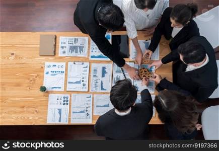 Top view hand holding gear by businesspeople wearing suit for harmony synergy in office workplace concept. Group of people hand making chain of gears into collective form with dashboard report papers.. Top view hand holding gear by group of businesspeople on table in harmony office