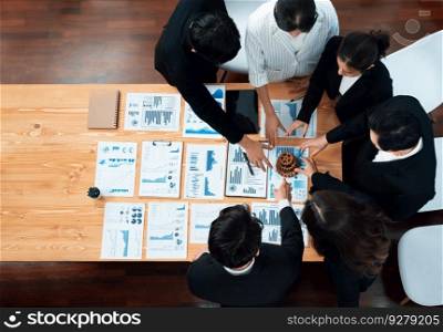 Top view hand holding gear by businesspeople wearing suit for harmony synergy in office workplace concept. Group of people hand making chain of gears into collective form with dashboard report papers.. Top view hand holding gear by group of businesspeople on table in harmony office