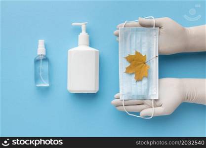 top view hands holding medical mask with autumn leaf liquid soap bottle