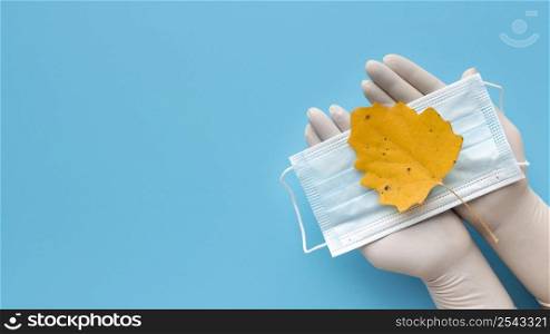 top view hands with gloves holding medical mask with autumn leaf