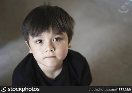 Top view head shot kid looking up with copy space, Candid young boy looking at camera with curiouse face, Child sitting on floor relaxing at home on weekend, Healthy and Positive children concept