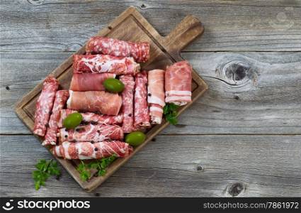 Top view horizontal image of various meats on serving board with ham, pork, beef, parsley, and olives on rustic wood.