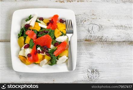 Top view image of a healthy fresh salad on plate with rustic white wooden boards underneath.