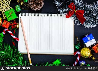 Top view image of Christmas festive decorations with empty notebook and pencil on black paper background, New Year concept.