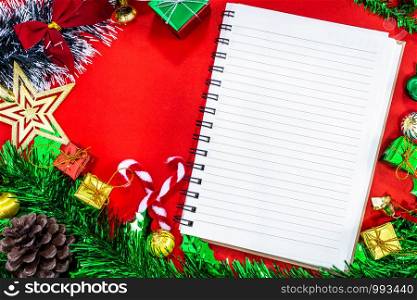 Top view image of Christmas festive decorations with empty notebook and pencil on red paper background, New Year concept.