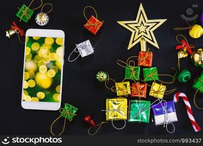 Top view image of Christmas festive decorations with empty smartphone,notebook and pencil on black paper background, New Year concept,yellow light Abstract circular bokeh