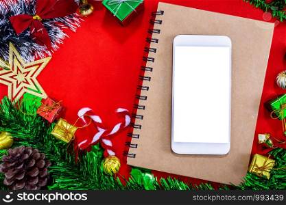 Top view image of Christmas festive decorations with empty smartphone,notebook and pencil on red paper background, New Year concept.