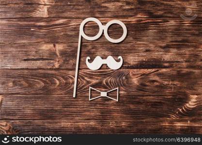 Top view image of fathers day composition with paper mustache, bow tie and glasses forming man face on wooden background. Fathers day concept