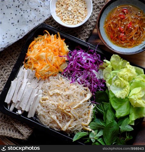 Top view ingredient food for fresh vegan rice paper rolls, a popular Vietnamese eating that healthy eating with colorful vegetables as carrot, violet cabbage, sausage, vermicelli, tofu, salad, herbs