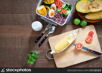 Top view kitchen table with lunch box, rice berry, boiled eggs, . Top view kitchen table with lunch box, rice berry, boiled eggs, corn, tomatoes and cutting board preparing food. Healthy lifestyle concept