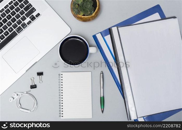 top view laptop folders coffee cup earphone spiral notepad pen against gray background