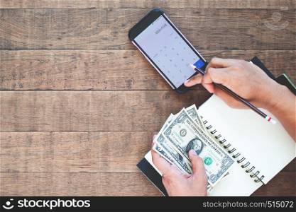 Top view man's hands holding US dollar bills and calculating on mobile phone