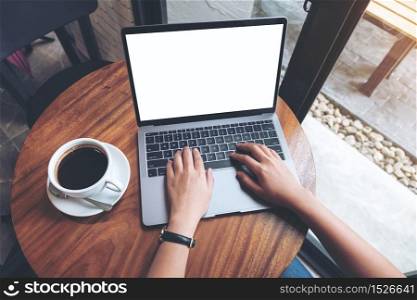 Top view mockup image of a woman using and typing on laptop with blank white desktop screen on wooden table in cafe