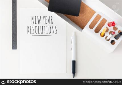 Top view new year resolutions 2020 paper note on modern office stationery on white table.pencil, notepad,ruler,pen and pencil box with plant.Mock up paper note for display of design or content
