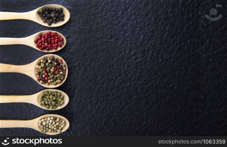 Top view of 5 types of peppercorn in a wooden spoon on a black background Healthy food concept