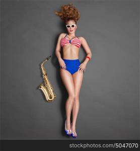 Top view of a beautiful pin-up girl in retro bikini and sunglasses, posing with a gold jazz saxophone on chalkboard background.