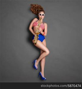 Top view of a beautiful pin-up girl in retro bikini and sunglasses, posing on chalkboard background and playing jazz saxophone.