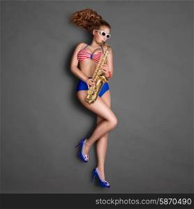 Top view of a beautiful pin-up girl in retro bikini and sunglasses, playing jazz saxophone on chalkboard background.