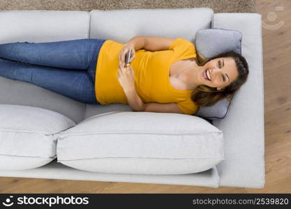 Top view of a beautiful young woman lying on a sofa and send text messages