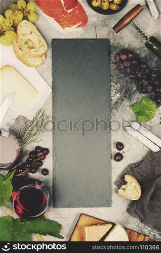 Top view of a blank chalk board for a wine list or menu with Wine and snack set. Variety of cheese, olives, prosciutto meat, baguette slices, black grapes and glasses of red wine over grey marble background, top view, copy space