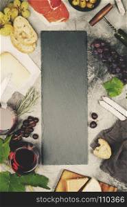 Top view of a blank chalk board for a wine list or menu with Wine and snack set. Variety of cheese, olives, prosciutto meat, baguette slices, black grapes and glasses of red wine over grey marble background, top view, copy space