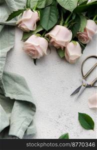 Top view of a bouquet of pink roses, scissors and fabric on a grey concrete background. Florist work place. Accessories for making bouquets and floral compositions.